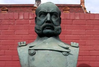 A bronze bust of Peruvian war hero, Miguel Grau Seminario, on a sandstone plinth against a red wall