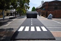 Sculpture made to look like a giant roll of bitumen with pedestrian crossing makings, unravelling like a rolled out carpet along a city street.