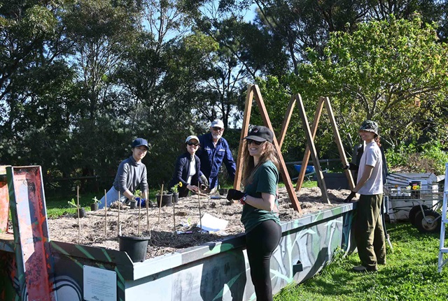 5 people stand around a raised planter bed in a community garden