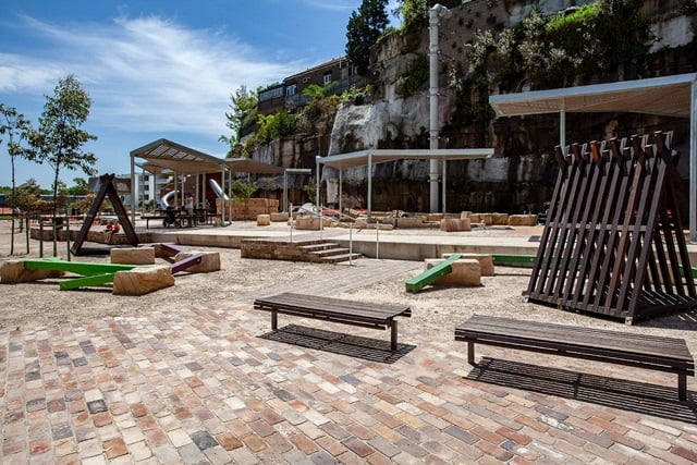 Two wooden benches . Two tall triangular shaped wooden structures resembling tents. shades and stepping stones in the background.