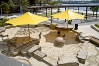 A large sandpit with 2 large yellow umbrellas giving shade in Pirrama Park Playground.