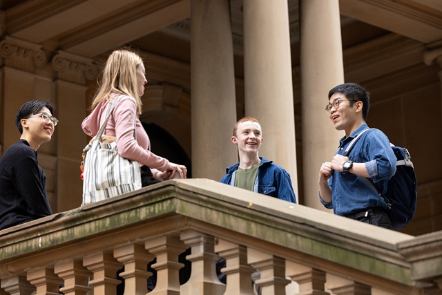Four young people stand at the top of a sandstone staircase outside Sydney Town Hall, smiling and talking to each other.